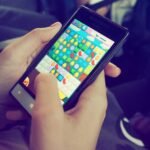 Hands holding a smartphone with a colorful puzzle game on the screen, displaying modern technology.