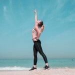 A woman performing a stretching exercise on a sunny beach in Dubai.